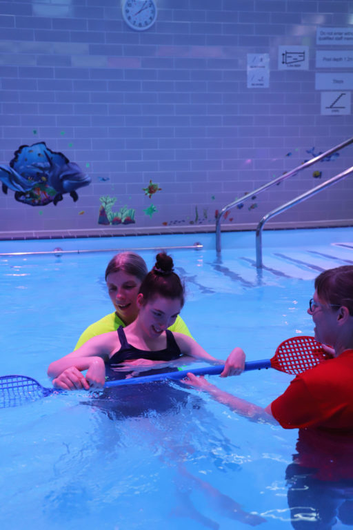 three people in a swimming pool, one of them is receiving hydrotherapy