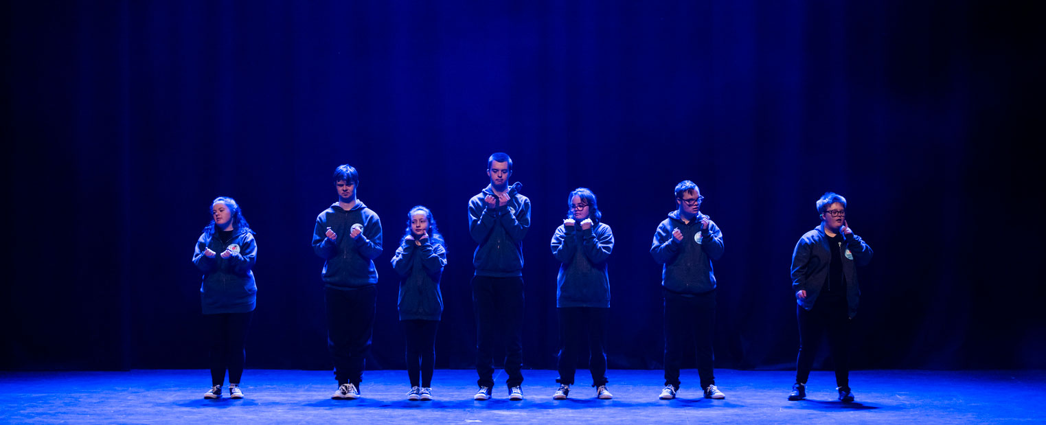 seven performers on stage standing under blue spotlights