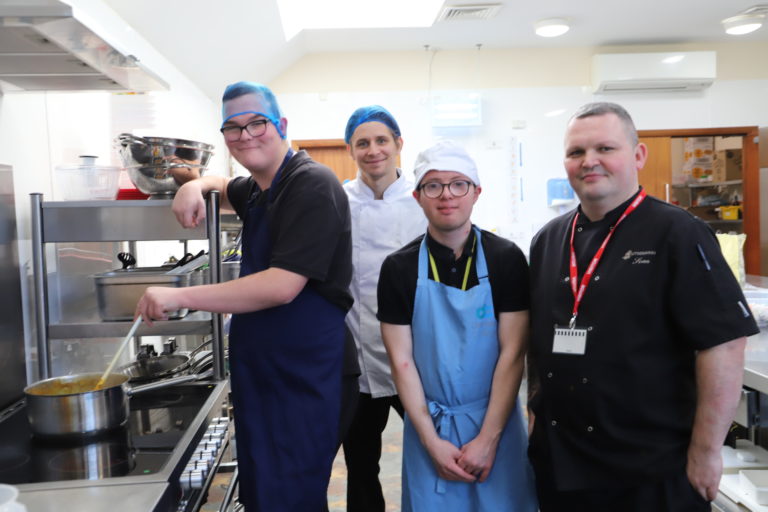 Student Ollie stirs a pot of curry while Marcus, teacher George and chef Sean look on.