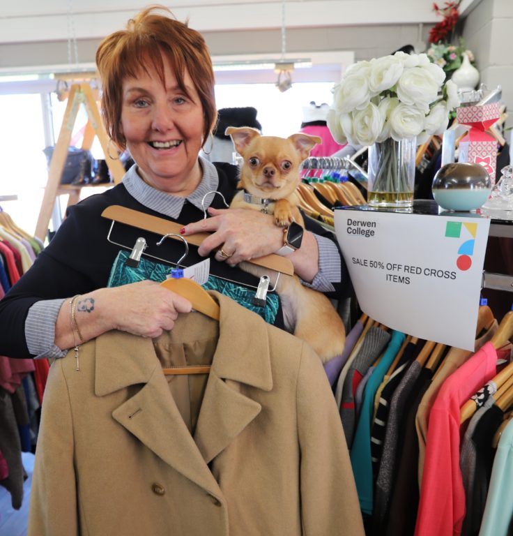 Shop assistant Karen holds her little dog Teddy and a bargain coats and gym legging which are on sale in the Vintage Advantage shop.