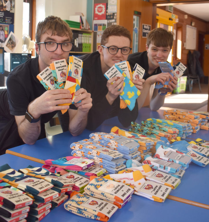 Three Retail students wearing smart black tops, sat at a table holding lots of colourful socks with piles of socks on the table in front of them.